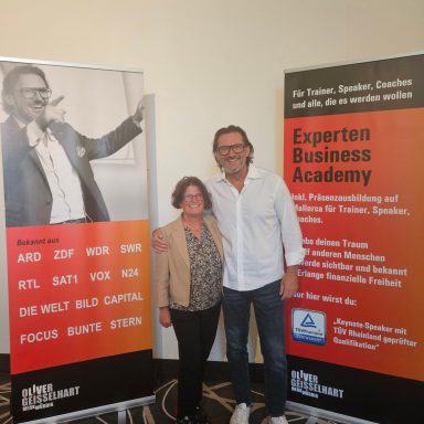 Zwei Personen stehen vor Bannern der Experten Business Academy und anderen Veranstaltungen.