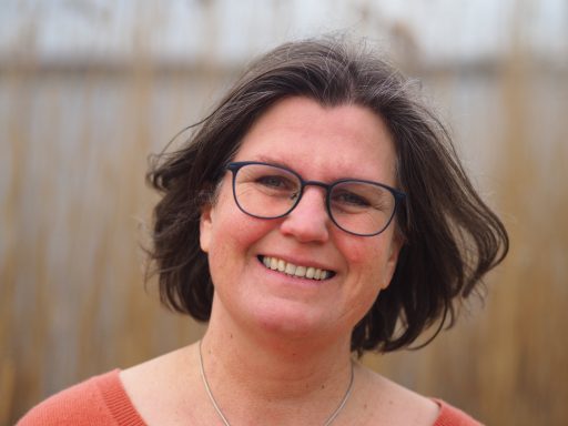 Lächelnde Frau mit Brille vor einem unscharfen Hintergrund von Schilf.